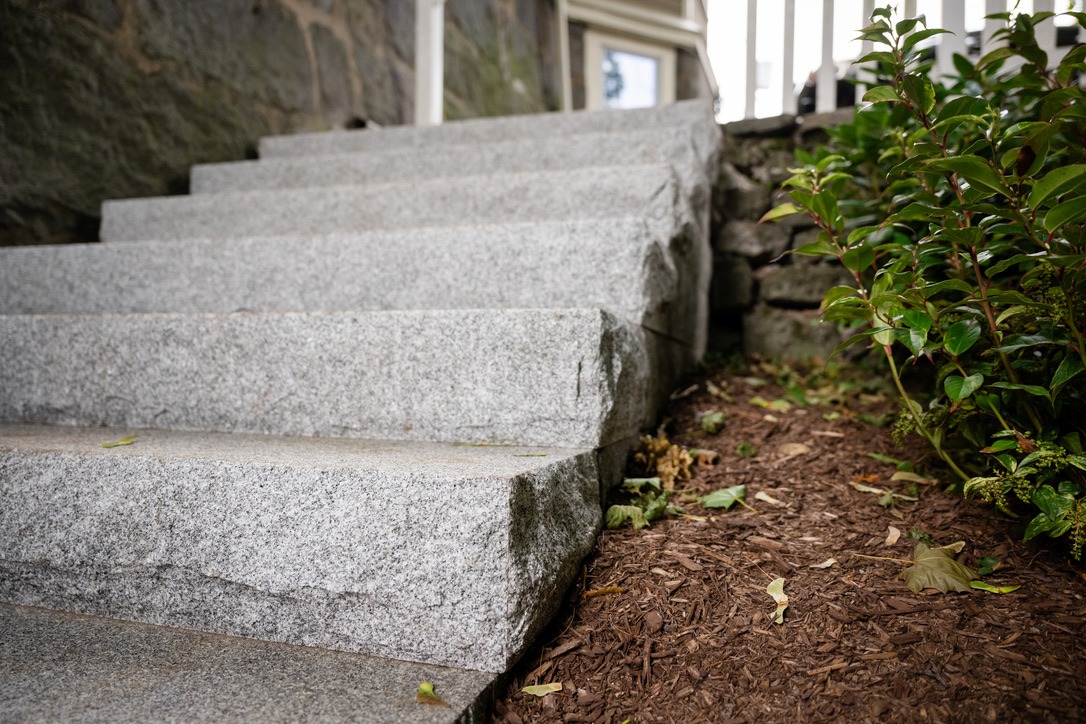 Stone steps lead upwards next to a stone wall and green shrubs. Fallen leaves are scattered on the ground, creating an autumn atmosphere.