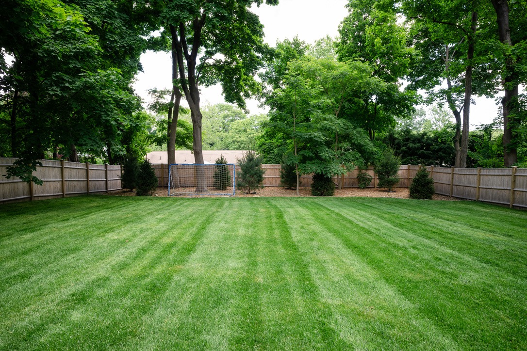 A well-maintained backyard features freshly mowed grass, a soccer goal, wooden fences, and surrounding lush green trees, creating a serene outdoor space.