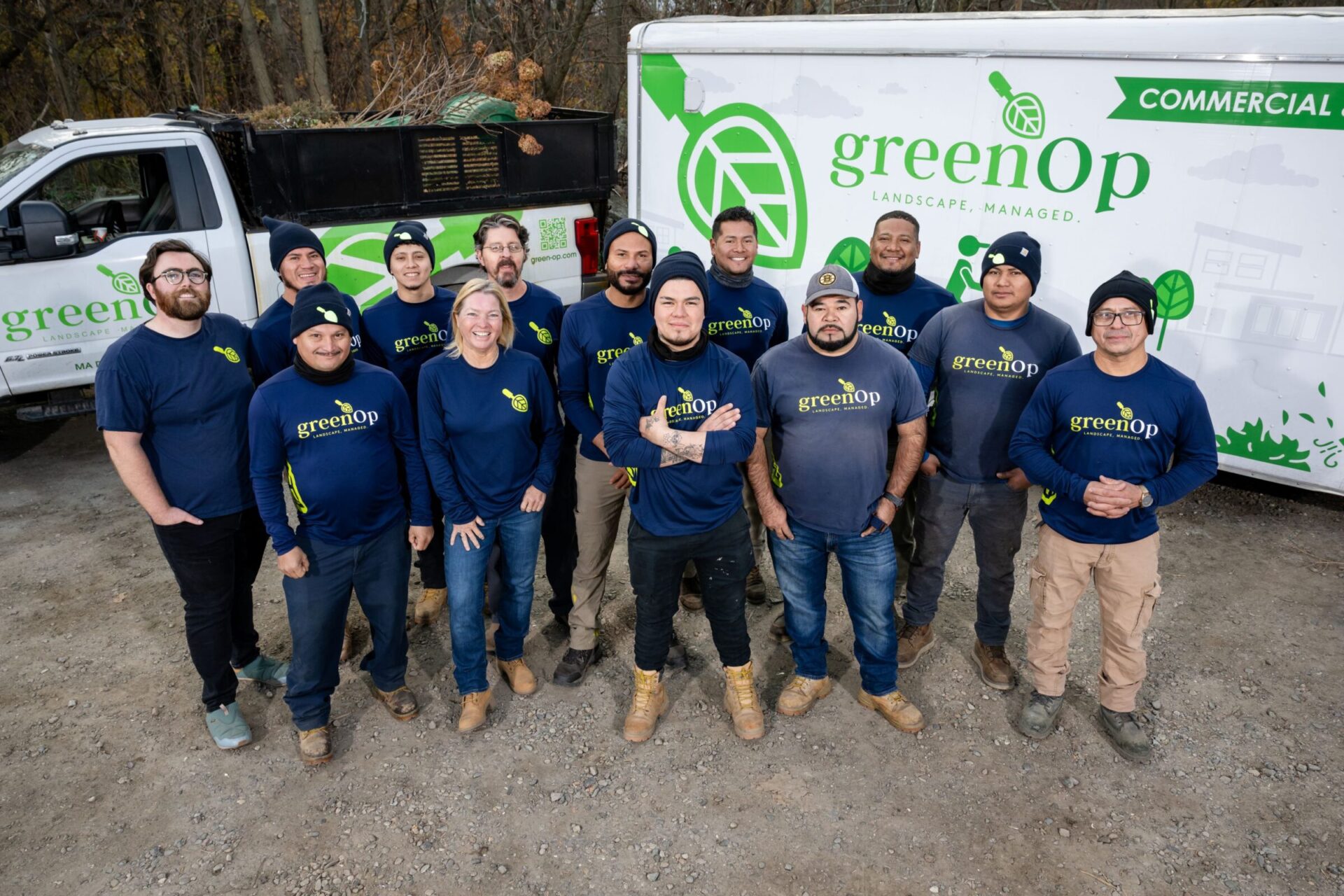 A group of people wearing matching "greenOp" shirts stand beside company-branded vehicles in a wooded outdoor setting.