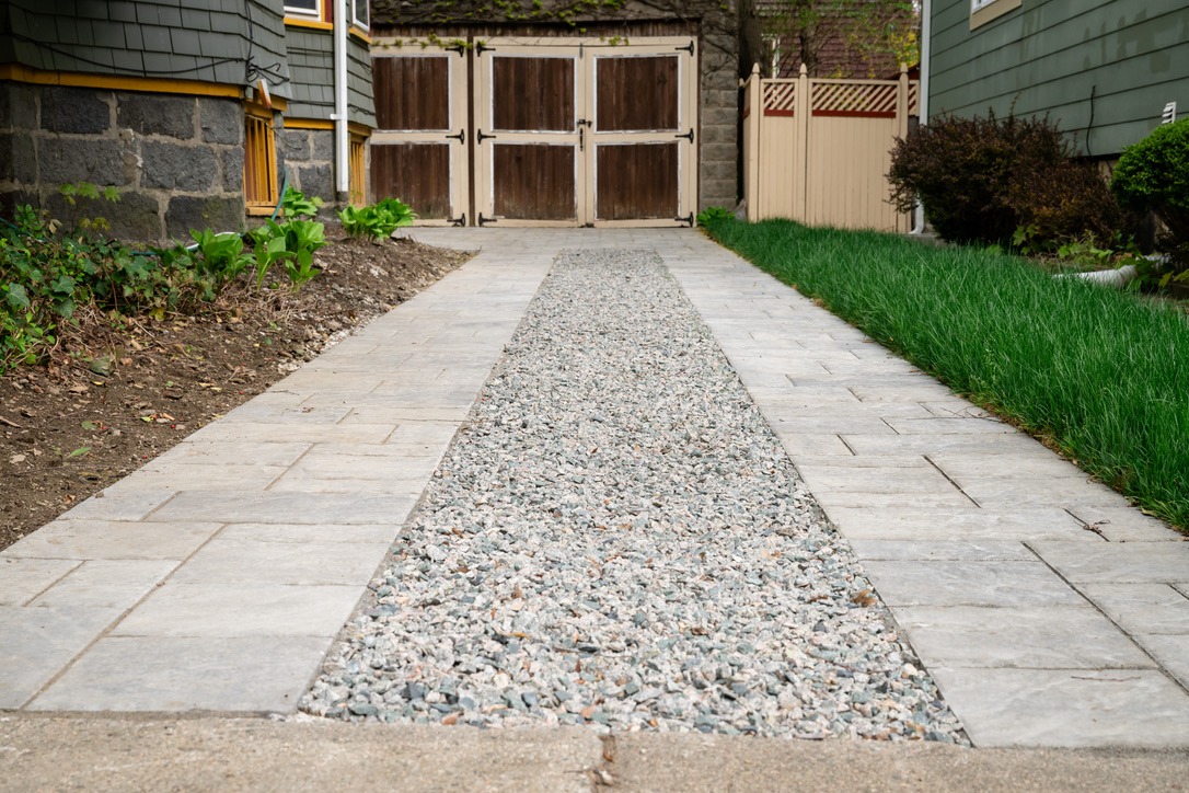 A narrow pathway leads to wooden double doors, bordered by green grass and a stone house wall on one side.